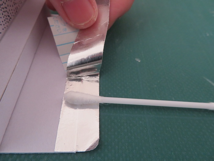両面テープのはくり紙を少しずつはがしながらアルミホイルを両面テープに貼る図
